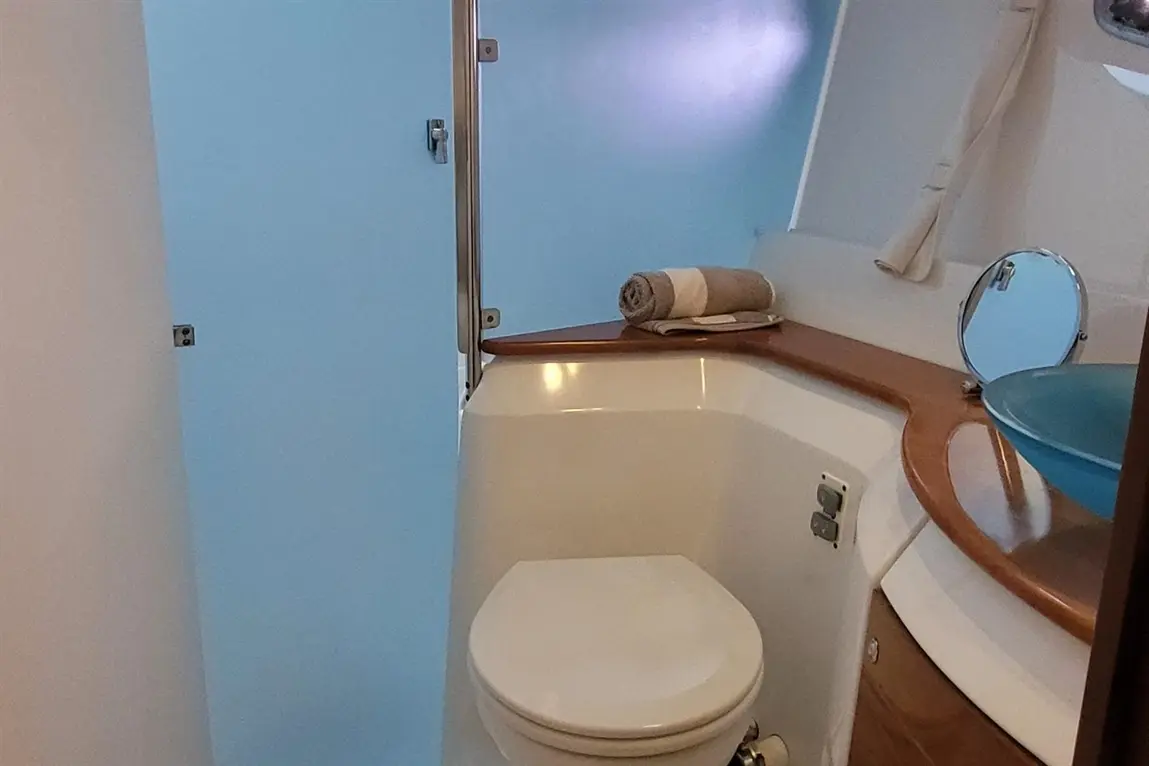 Nautical bathroom with a white toilet, blue basin, rolled towel, and light blue walls, providing a clean, bright atmosphere.